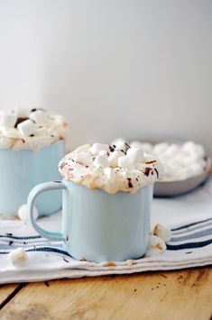 two mugs filled with hot chocolate and marshmallows sitting on a table