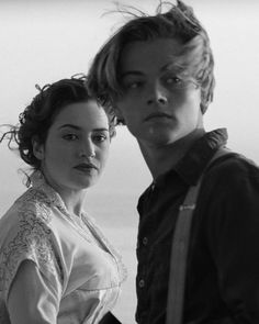 a man standing next to a woman on top of a beach near the ocean in black and white