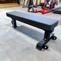 a black bench sitting in a garage next to some red dumbbells and other exercise equipment