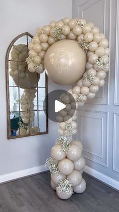 a balloon arch with white balloons hanging from it's sides in front of a mirror