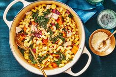 a pot filled with pasta and vegetables on top of a blue cloth next to two spoons