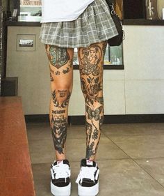 a woman with tattoos on her legs and leggings is standing in front of a counter