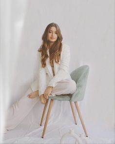 a woman sitting on top of a chair in front of a white wall with her legs crossed