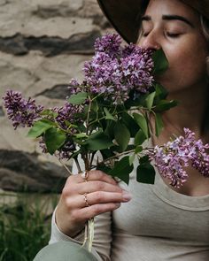 a woman in a hat smelling some purple flowers