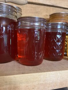 several jars filled with liquid sitting on top of a wooden shelf next to each other