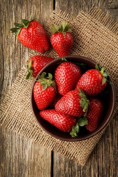 a bowl full of strawberries sitting on top of a wooden table with burlocks