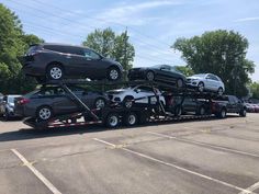 a car carrier with cars on it's back in a parking lot next to trees