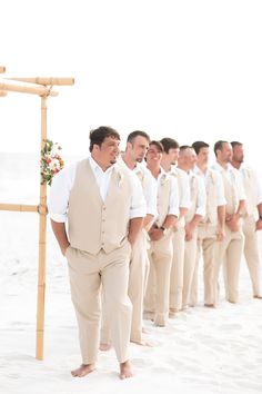 a group of men standing next to each other in front of a wooden structure on the beach