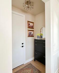 a hallway with white walls and wooden flooring next to a black chest of drawers