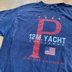 This piece is a vintage Ralph Lauren Polo Sport t-shirt from 1996. This dark navy blue tee has a big spell out on the front for the 1996 12 Metre Yacht Challenge Regatta. The shirt itself is made in the USA by Ralph Lauren from 100% cotton with a single stitch construction in a size XL. A very rare piece and would be an excellent addition to any Polo or vintage wardrobe. This piece is in good vintage condition with regular wear and fading from age. There are some splotches of faint bleach stains Blue Nautical Crew Neck T-shirt, Nautical Navy Short Sleeve T-shirt, Navy Nautical Short Sleeve T-shirt, Crew Neck Graphic T-shirt For Sailing, Crew Neck T-shirt With Graphic Print For Sailing, Vintage Navy Short Sleeve T-shirt, Vintage Navy T-shirt With Short Sleeves, Vintage Blue Crew Neck T-shirt, Crew Neck Graphic Print Top For Sailing