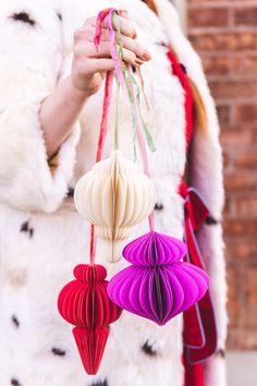 a woman holding three paper lanterns in her hands and wearing a fur coat behind her