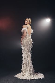 a woman in a white feathered dress standing on a black background with lights behind her