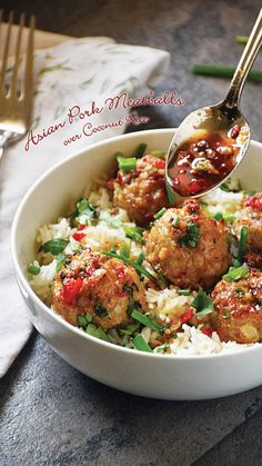 a white bowl filled with meatballs and rice on top of a table next to silverware