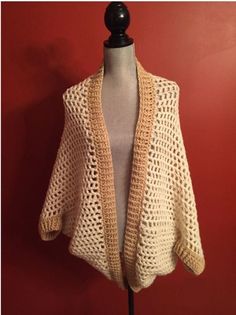 a crocheted shawl on a mannequin with a red wall in the background