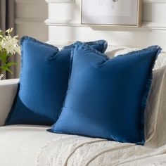 two blue pillows sitting on top of a white couch next to a vase with flowers