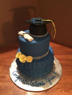 a graduation cake with blue icing and yellow flowers on top is sitting on a wooden table