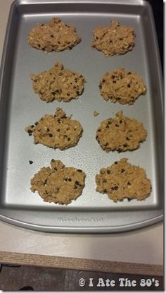 six cookies on a cookie sheet ready to be baked in the oven, with chocolate chips and oatmeal toppings