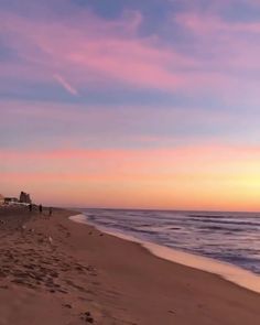 people walking on the beach at sunset or sunrise time with pink and blue sky in background