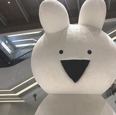 a large white teddy bear in the middle of an indoor mall with escalators