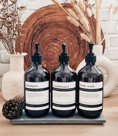 three bottles of liquid sitting on top of a table next to a pine cone and vase