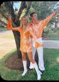 a man and woman dressed in orange standing next to a tree with their arms outstretched