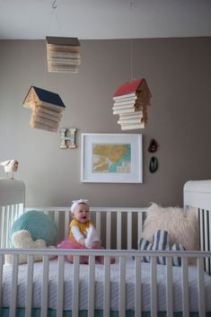 a baby sitting in a crib with books hanging from the ceiling above her head