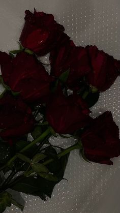 a bunch of red roses sitting on top of a white table covered in water droplets