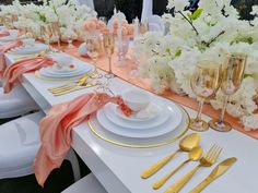 the table is set with gold and white plates, silverware, napkins, and flowers