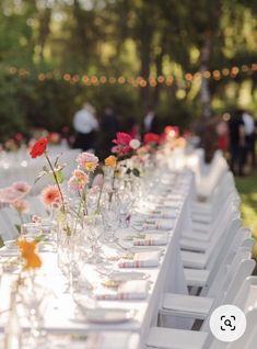 a long table is set up with white chairs and flowers in vases on the tables