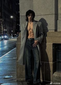 a shirtless man leaning against a wall in the city at night with his hands on his hips