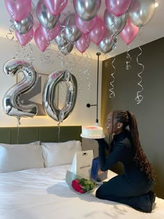 a woman sitting on top of a bed next to balloons