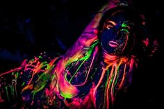 a woman covered in neon paint laying on the ground with her hands behind her head