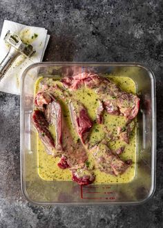 raw meat in a plastic container with sauce on the side and utensils next to it