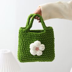 a hand holding a green crocheted bag with a flower on it's handle