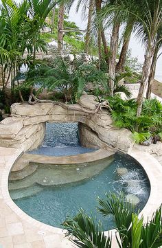 an outdoor swimming pool surrounded by plants and rocks with a waterfall in the middle,