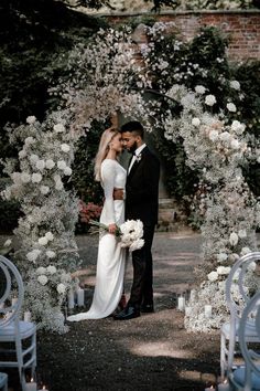 a bride and groom standing in front of an archway with white flowers