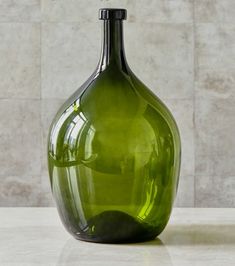 a green glass vase sitting on top of a white counter next to a tiled wall