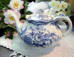 a blue and white tea pot sitting on top of a doily next to flowers