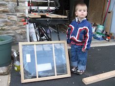 a young boy standing next to a window in front of a building with tools on the ground