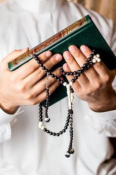 a man in a white shirt is holding a book with rosarys on his hands