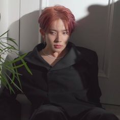 a man with red hair sitting next to a plant