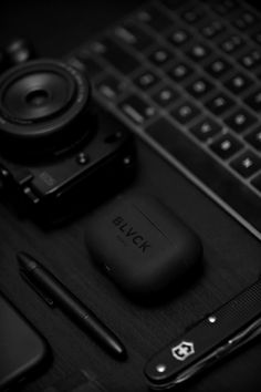 a black and white photo of a desk with a laptop, camera, cell phone and pen