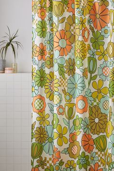 a shower curtain with colorful flowers on it in a white bathroom next to a potted plant