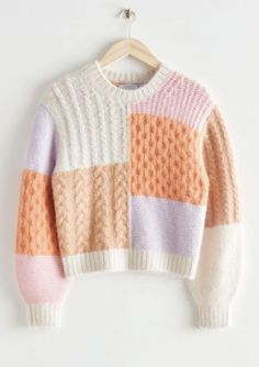 an orange, pink and white sweater hangs on a hanger against a white wall