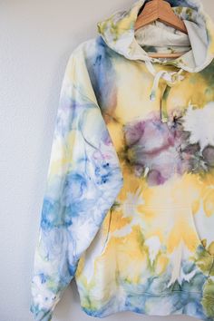 a yellow and blue tie dye hoodie hanging on a white wall with a wooden hanger