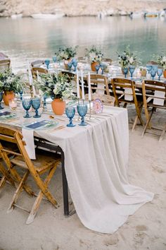 an outdoor table set up with blue vases and greenery on the beach for a wedding reception