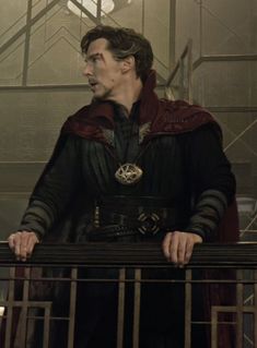 a man standing on top of a balcony next to a metal railing and wearing a red cape