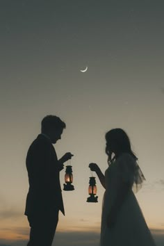 the bride and groom are holding lanterns in their hands at night with the moon behind them