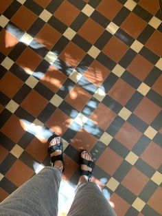 a person standing on a checkered floor with their feet propped up in sandals and jeans