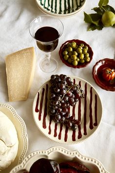 a table topped with plates and bowls filled with food next to glasses of red wine